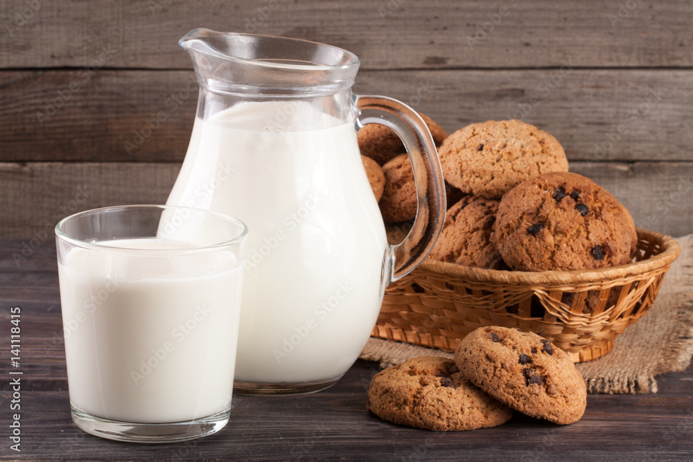 jug and glass of milk with oatmeal cookies in a wicker basket on a wooden background jug and glass of milk with oatmeal cookies in a wicker basket on a wooden background