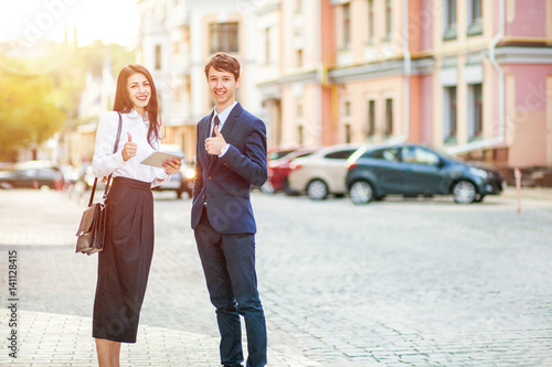Young happy handsome business man and woman gesturing thumb up. Business success concept in city background.