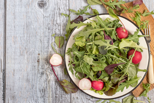  Fresh green salad with radish. Herbs such as chard, lettuce, beet leaves on a white metal plate on a kitchen cutting board.