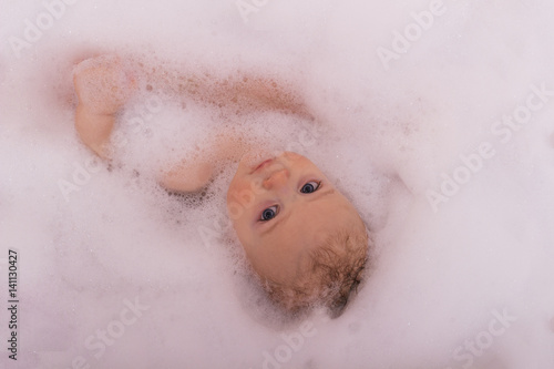 A baby in a bathtub in soap foam looking at camera