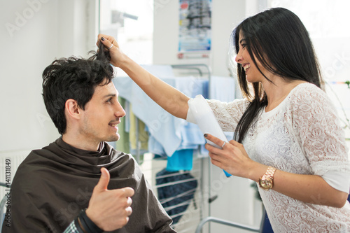 Happy young male client showing thumb up to his female hairdresser at hair salon.