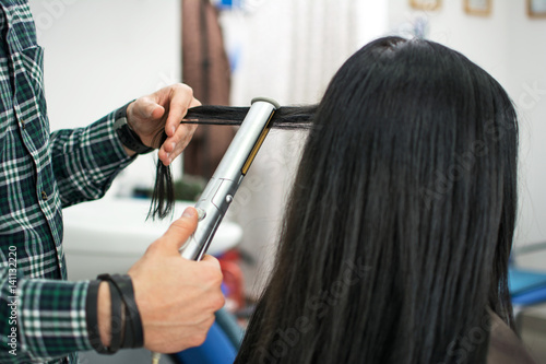 Close up of a hairdresser straightening long black hair with hair irons.