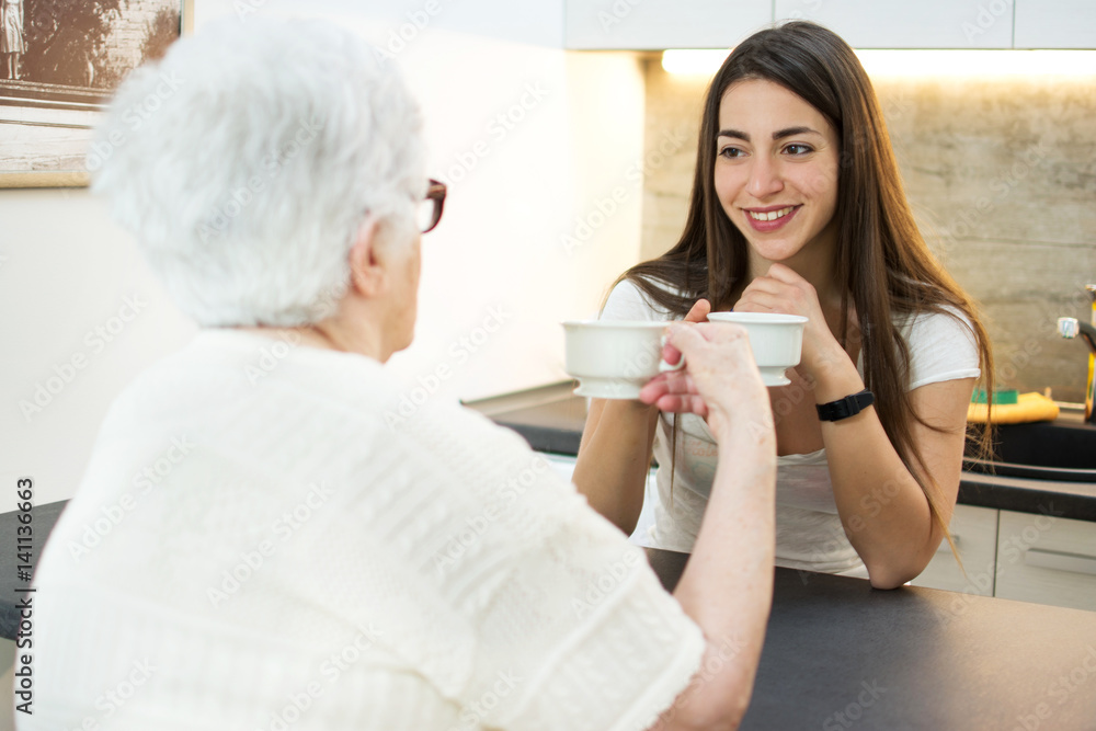 Granddaughter having a cup of coffee with her grandmother in the kitchen. Granddaughter having a cup of coffee with her grandmother in the kitchen.