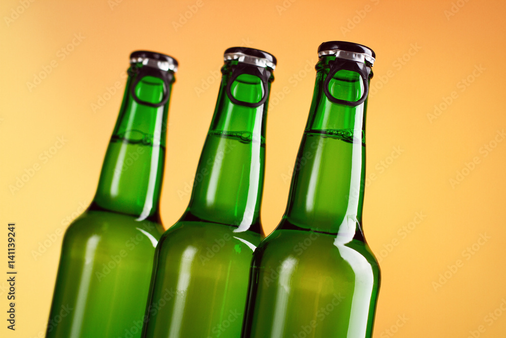 Three green beer bottles isolated over orange background