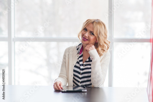 A beautiful young blond woman siting at the table using a laptop.