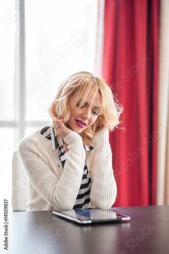 A beautiful young blond woman siting at the table using a laptop.