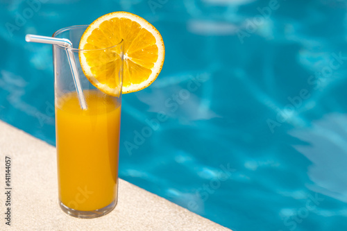 Glass of orange juice with orange slice near the swimming pool