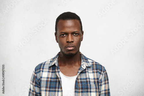 Portrait of handsome young African American male dressed in blue checkered shirt over white t-shirt looking at camera with serious and confident expression on his face. People and lifestyle concept