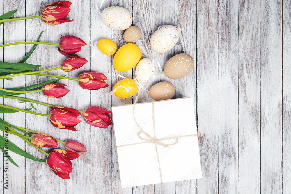 Easter background. Colored easter eggs and red tulips on wooden background. Top view.
