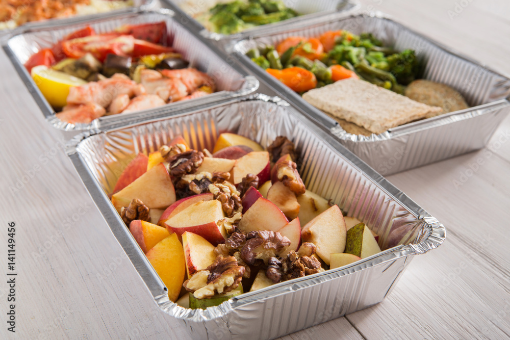 Healthy food take away in foil boxes on wood background Healthy food take away in foil boxes on wood background