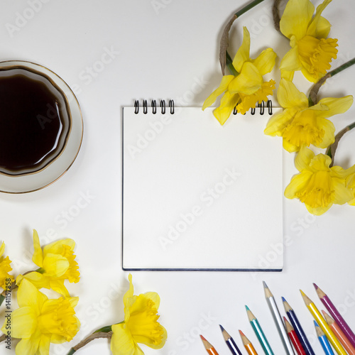 Cup of coffee and a saucer, daffodils and pencils on a white background