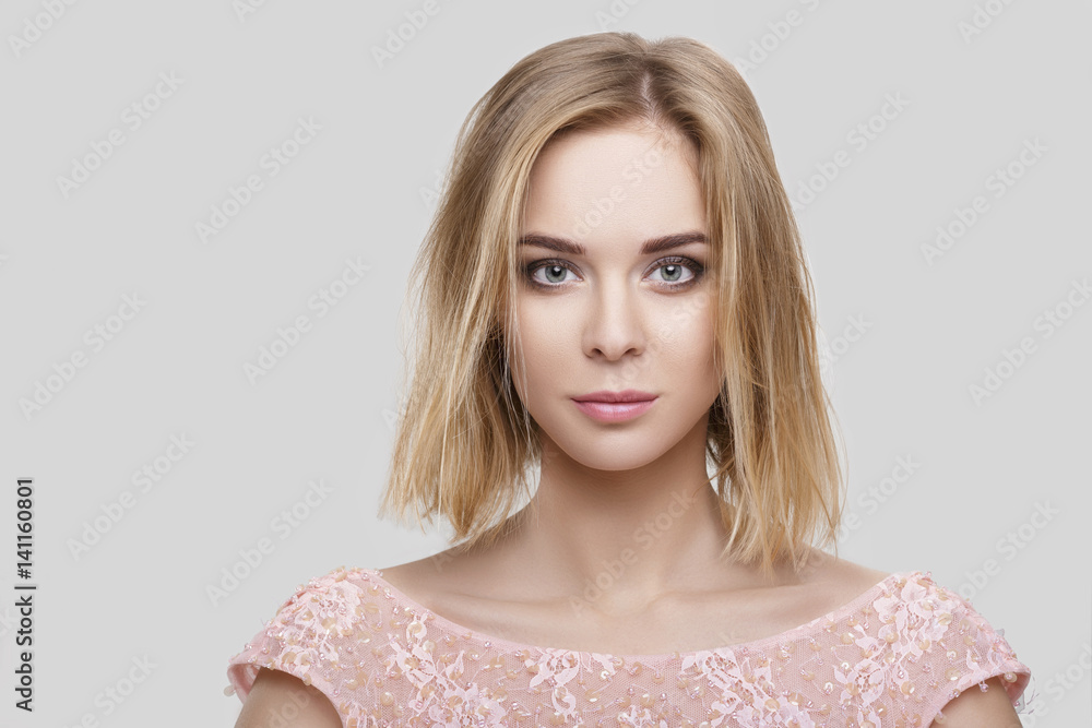 portrait of beautiful blond woman with short hair in pink cocktail dress on grey background