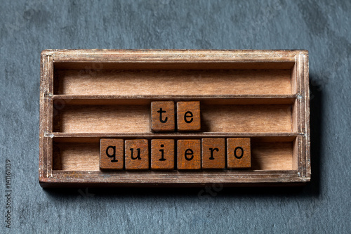 Te quiero. I love you in Spanish language. Vintage box, wooden cubes phrase with old style letters. Gray stone textured background. Close-up, up view, soft focus photo