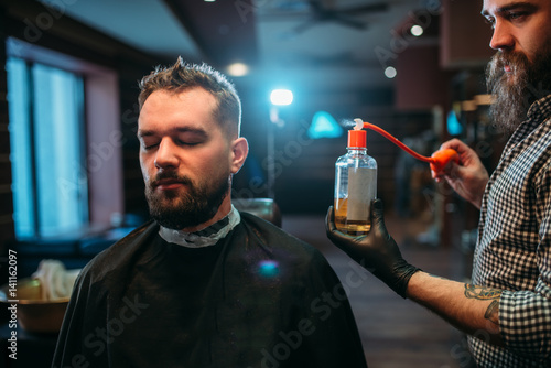 Foto Barber splashing client face by aftershave lotion