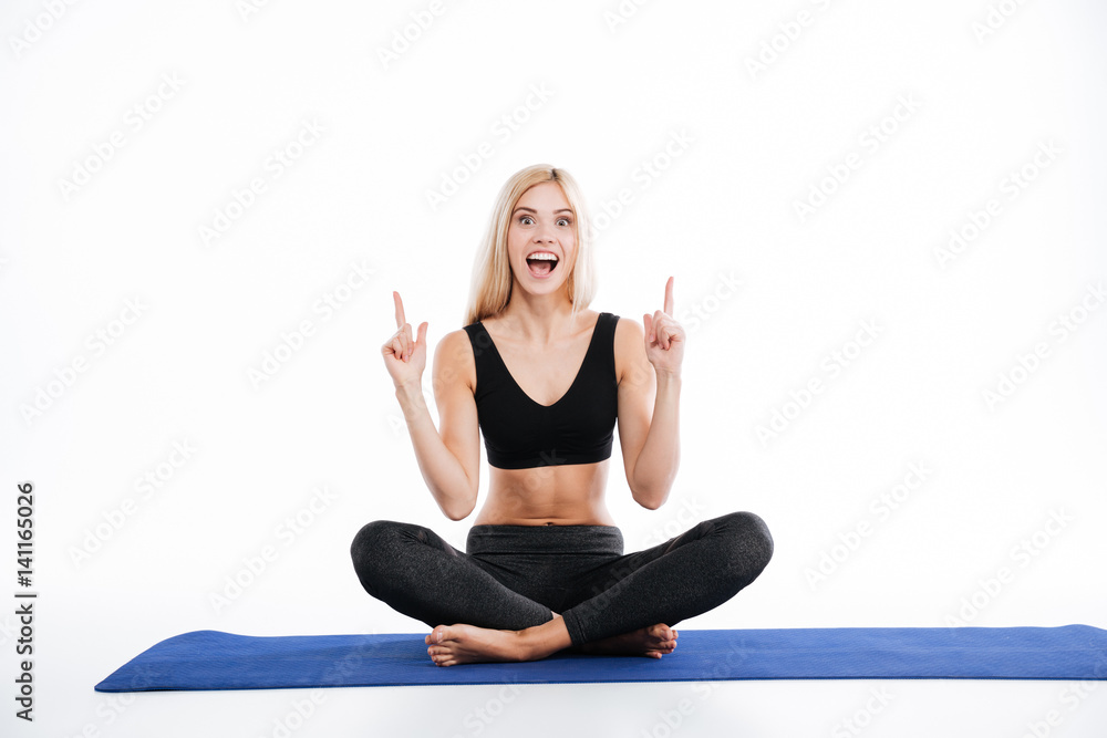 Smiling fitness woman sitting make yoga exercises pointing.