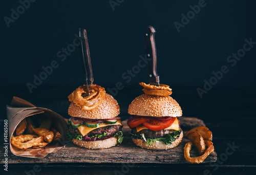 Two mouth-watering, delicious homemade burger used to chop beef. on the wooden table. The burgers are inserted knives.