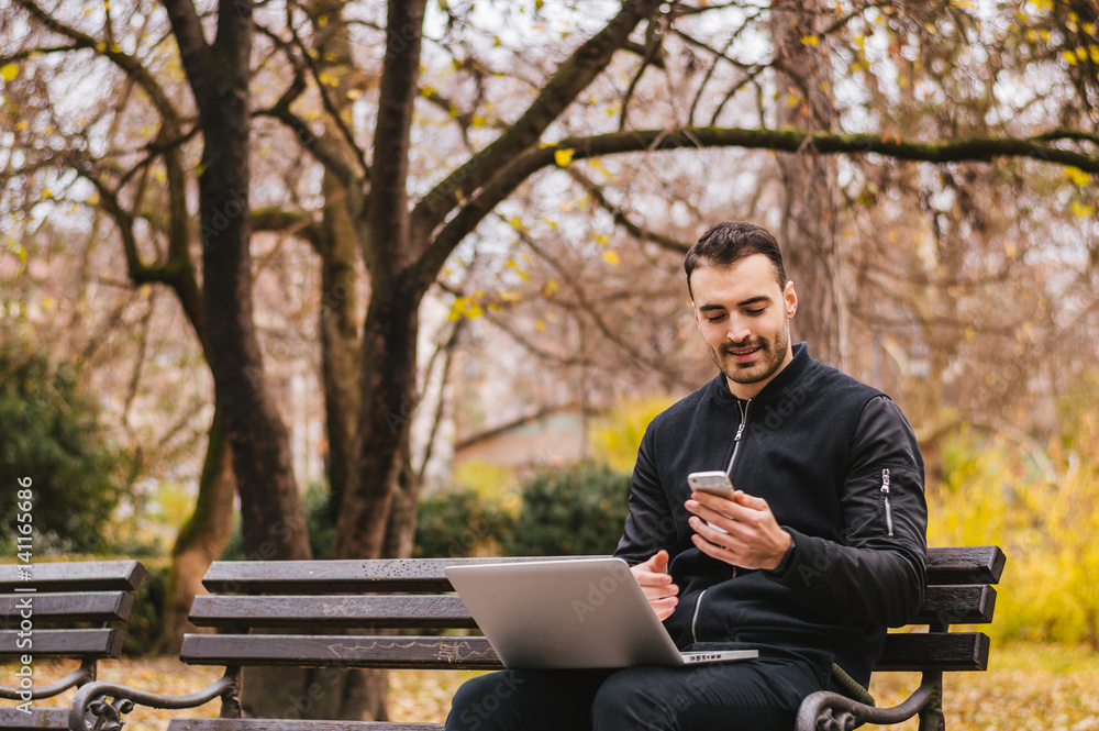 Handsome young man sitting on a wooden bench working outdoors Handsome young man sitting on a wooden bench working outdoors