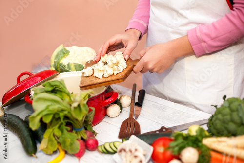 Woman putting raw cauliflower in the kitchen dish