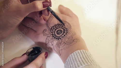 Woman making mehendi on a hand with henna photo