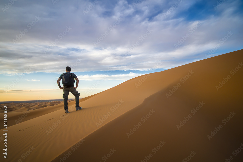 Man walking alone on the dunes of the Sahara Desert in Merzouga admiring the sunset  - Morocco