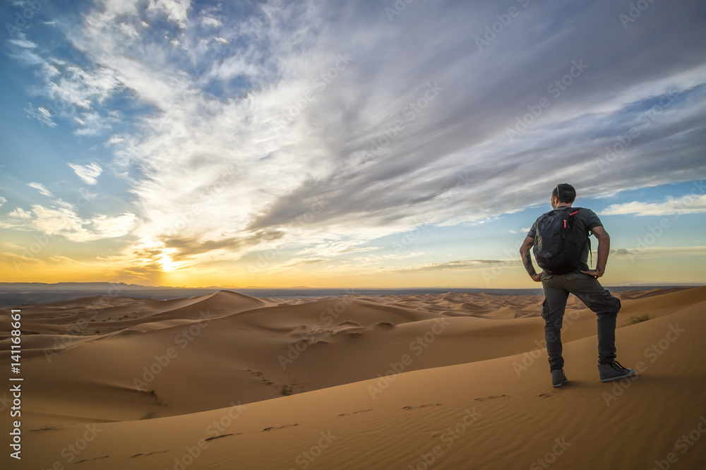 Man walking alone on the dunes of the Sahara Desert in Merzouga admiring the sunset - Morocco Man walking alone on the dunes of the Sahara Desert in Merzouga admiring the sunset - Morocco