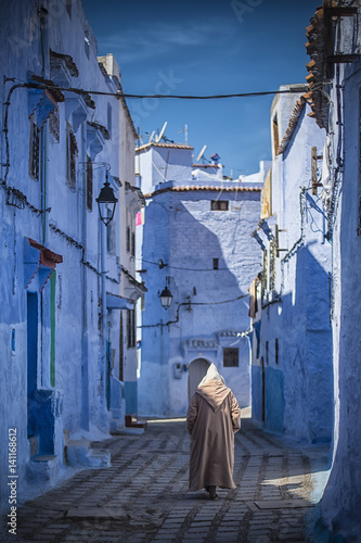 Man with a traditional dress is walking in the blue medina of Chefchaouen, Morocco. © Travel Wild