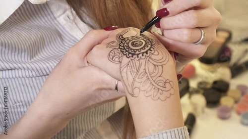 Closeup of woman making mehendi on a hand with henna photo