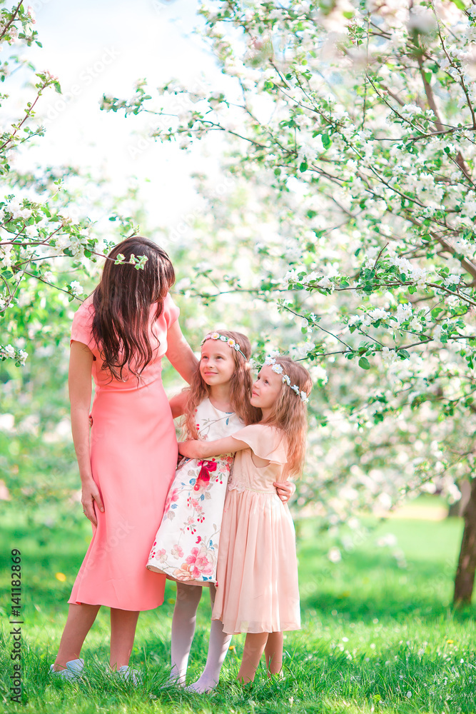 Adorable little girls with young mother in blooming apple garden on Easter Adorable little girls with young mother in blooming apple garden on Easter
