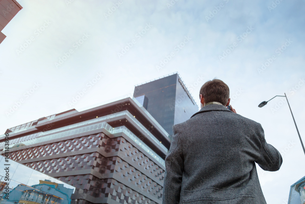 A young man in a coat makes an anonymous phone call standing near the business center. A young man in a coat makes an anonymous phone call standing near the business center.