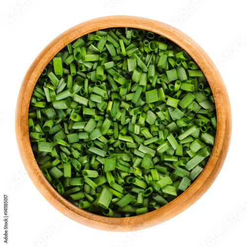Chopped chives in wooden bowl. Fresh green edible herb of Allium schoenoprasum, used as an ingredient for fish, potatoes and soups. Isolated macro food photo close up from above on white background.