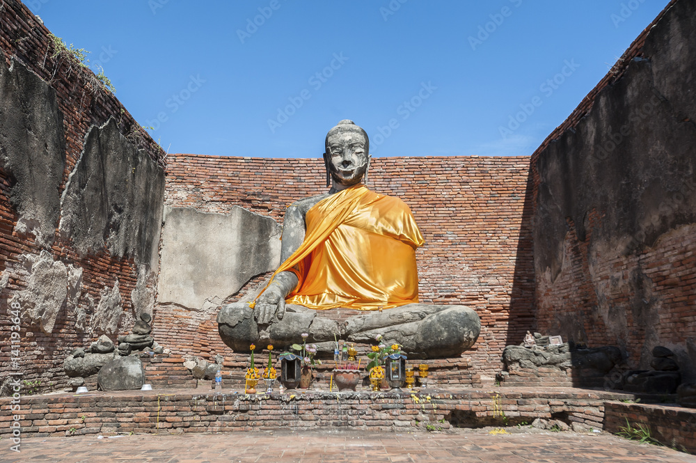 Fototapeta premium Large stone Buddha statue at the partially restored ruin of Wat Worachet Tharam in the ancient city of Ayutthaya, Thailand