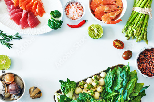 Top view of salmon and tuna sashimi, cooked shrimps, clamps, brown rice, asparagus and spinach over white background. Ingredients for healthy dinner. 
