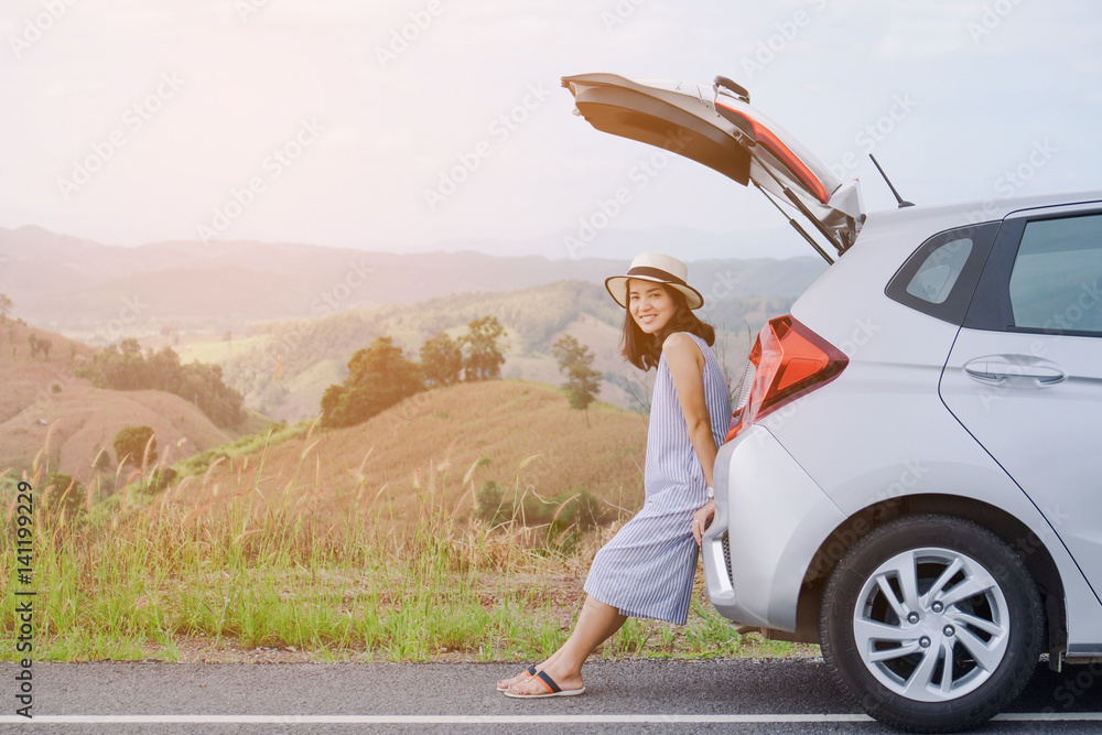 Fototapeta premium Woman traveler sitting on hatchback car with mountain background in vintage tone