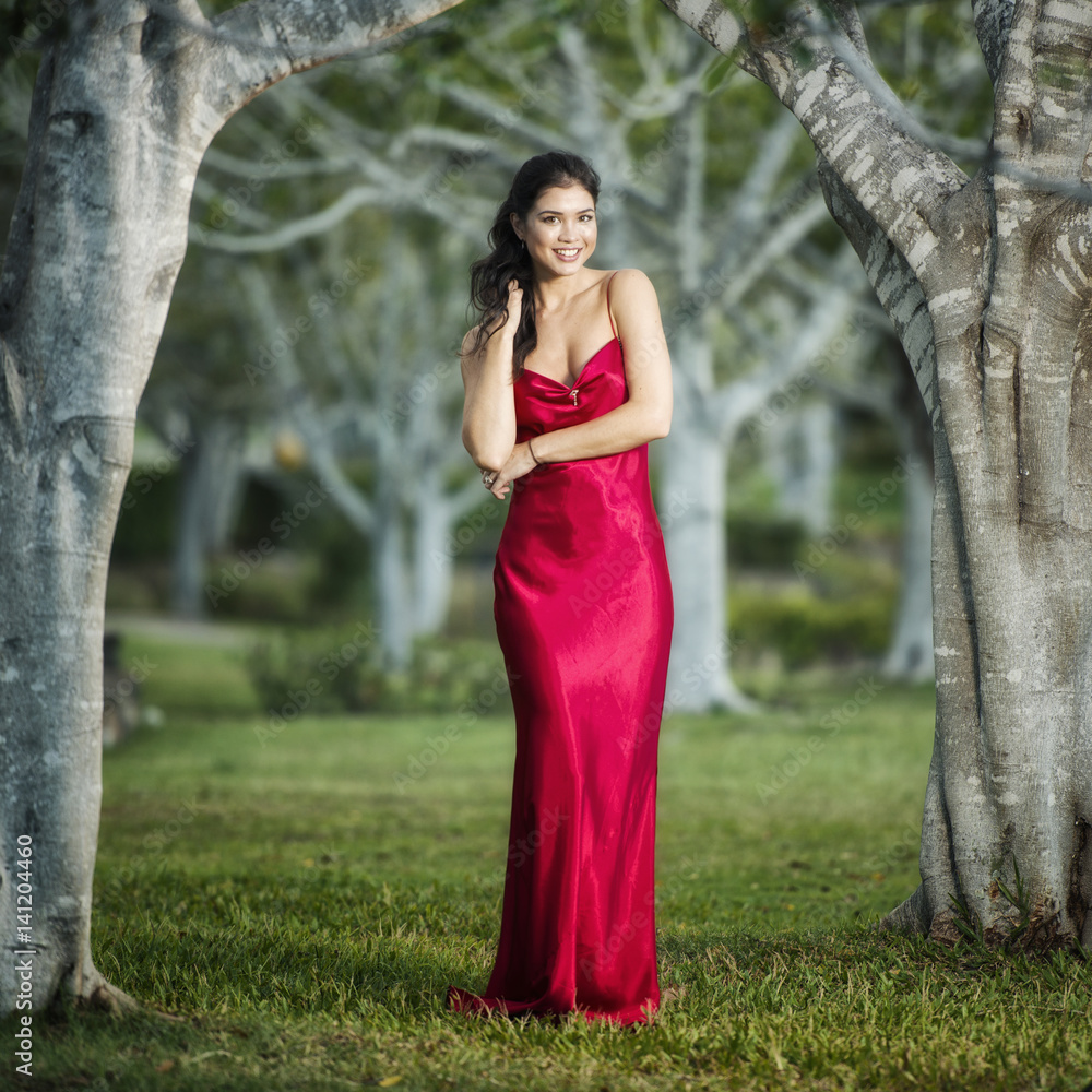 Beautiful young woman in the gardens wearing a long silk red dress. Beautiful young woman in the gardens wearing a long silk red dress.