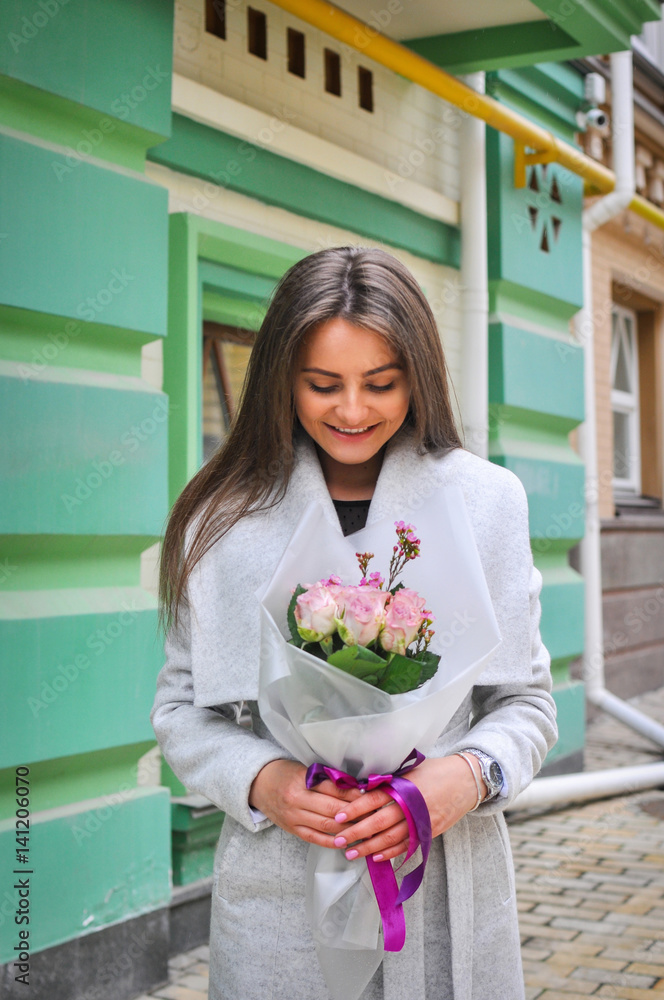 Beautiful young woman with flowers bouquet at city street. Spring portrait of pretty female