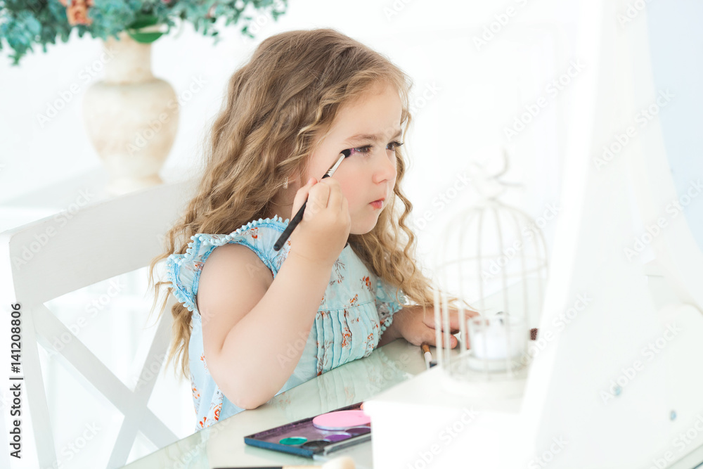 Cute little girl applying make up looking into mirror. Little fashionista girl playing with her mother`s cosmetics. Adorable child indoors