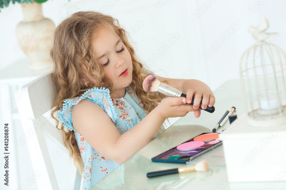 Cute little girl applying make up looking into mirror. Little fashionista girl playing with her mother`s cosmetics. Adorable child indoors Cute little girl applying make up looking into mirror. Little fashionista girl playing with her mother`s cosmetics. Adorable child indoors