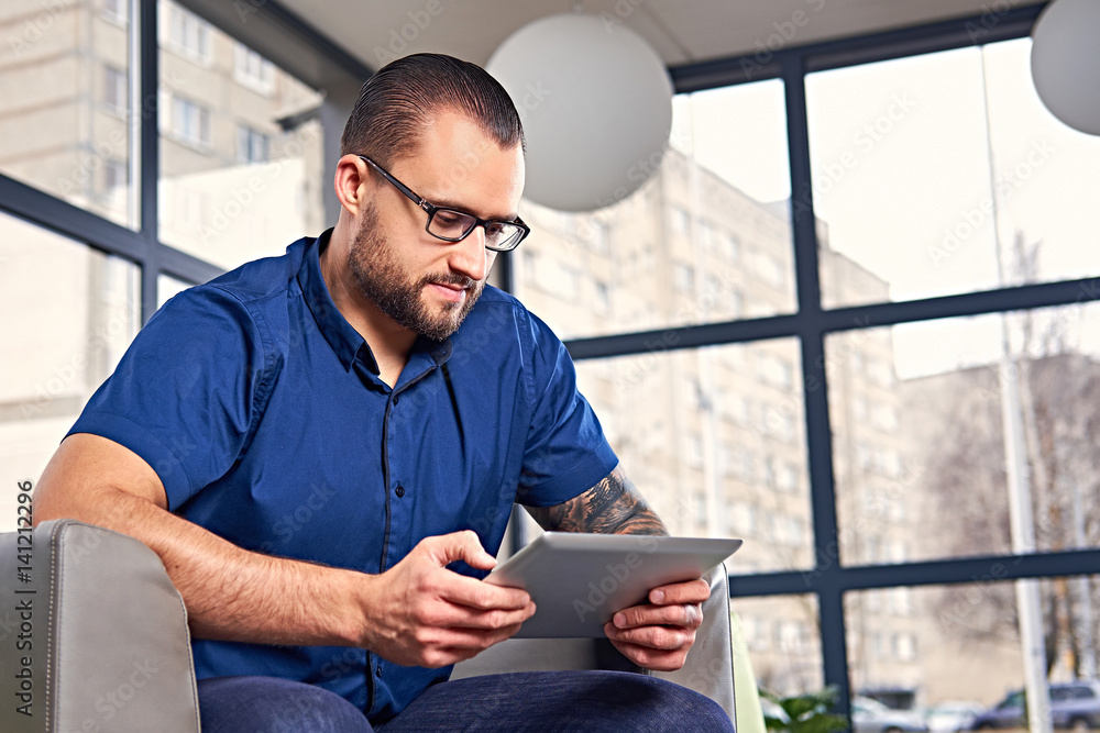 Bearded male in eyeglasses using a tablet PC. Bearded male in eyeglasses using a tablet PC.