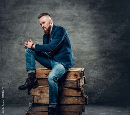 Redhead bearded hipster male posing on a wooden box.