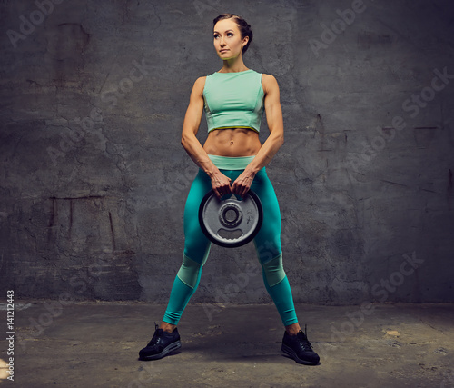 Sporty female working out with barbell weight over grey background.