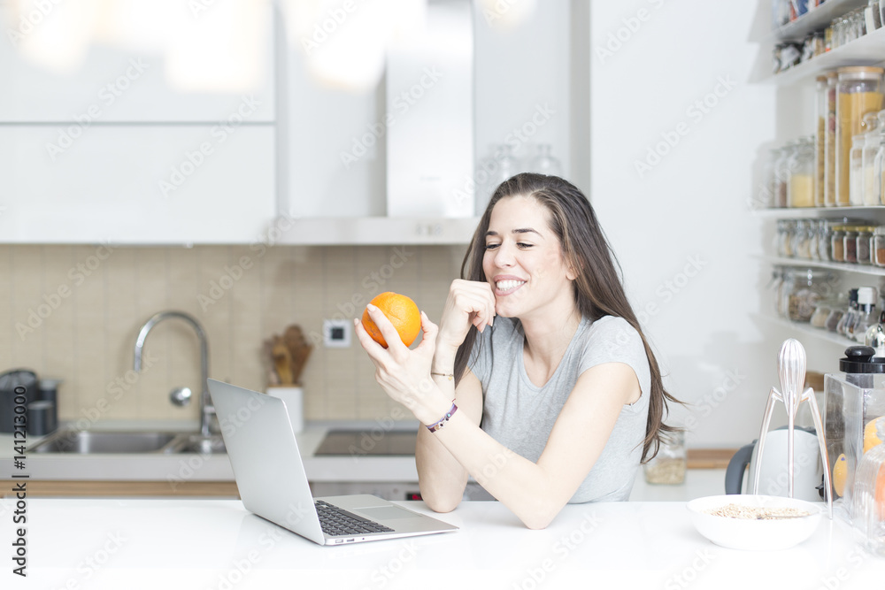 Morning scene. Beautiful woman holding orange in front of laptop Morning scene. Beautiful woman holding orange in front of laptop