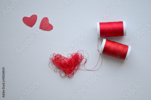 Heart in shape of red buttons, needle and yarn on unbleached fabric.