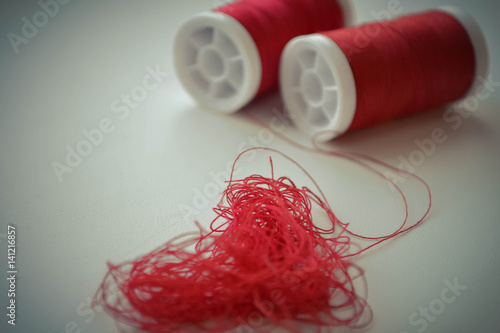 Heart in shape of red buttons, needle and yarn on unbleached fabric.