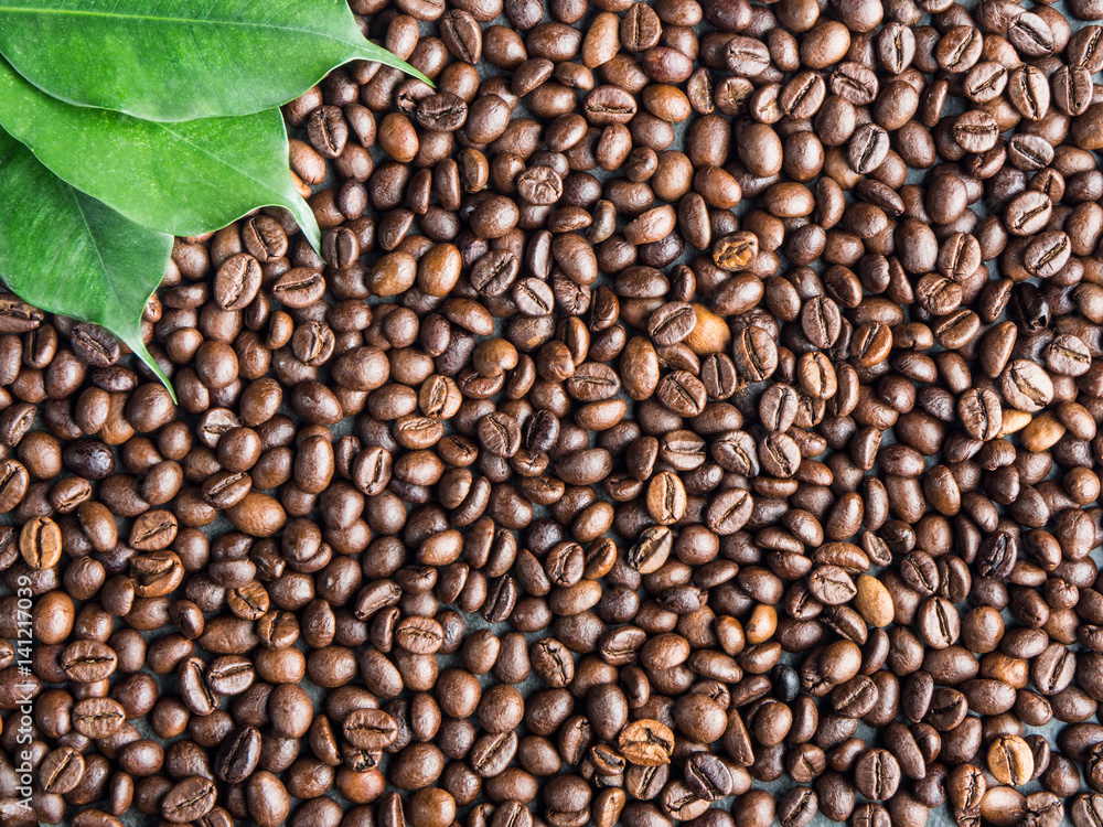 Roasted coffee beans background with green leaves, captured from top view with sharp focus Roasted coffee beans background with green leaves, captured from top view with sharp focus