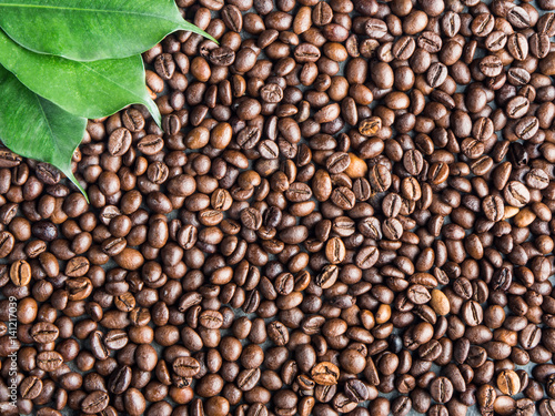 Roasted coffee beans background with green leaves  captured from top view with sharp focus