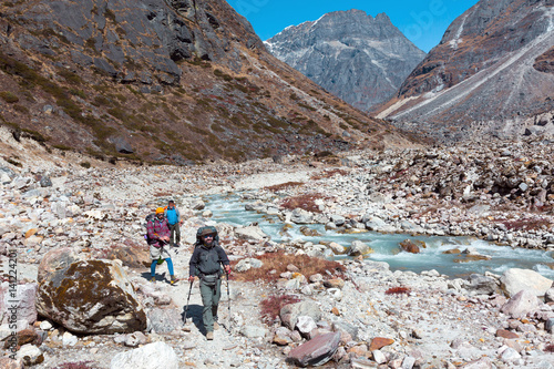 Three Hikers walking on rocky Footpath along wild Mountain River