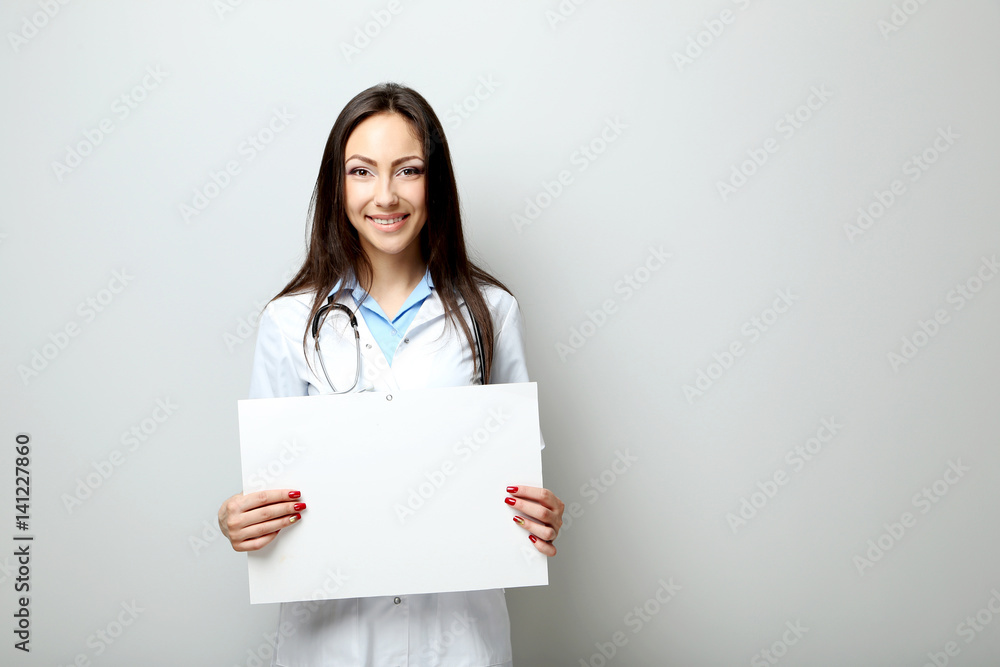 Portrait of young medical doctor with sheet on blank paper on a grey background