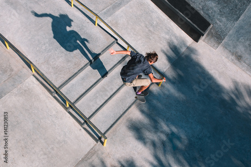 Young man - skater jump on his skateboard through stairs in a concrete skatepark
