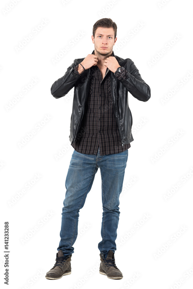 Handsome young man adjusting collar of black leather jacket looking at camera. Full body length portrait isolated over white studio background. Handsome young man adjusting collar of black leather jacket looking at camera. Full body length portrait isolated over white studio background.