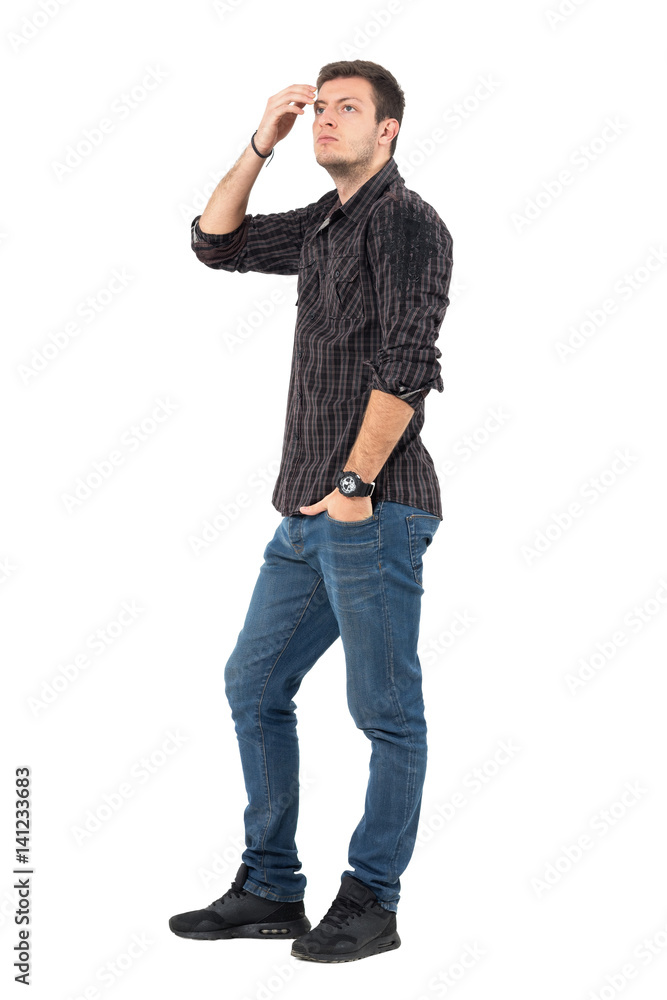 Side view of casual young man in jeans and plaid shirt adjusting hair with hand looking up. Full body length portrait over white studio background. Side view of casual young man in jeans and plaid shirt adjusting hair with hand looking up. Full body length portrait over white studio background.
